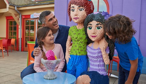 Family sat with LEGO Friends LEGO model outside Heartlake Cafe