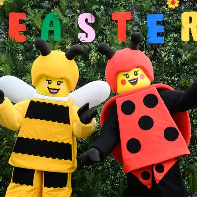 Bumblebee Girl And Lady Bug Girl at LEGOLAND Windsor in front of a foliage background with an Easter sign made out of LEGO