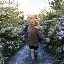 Girl smiling and running through snow covered trees at LEGOLAND at Christmas at the LEGOLAND Windsor Resort