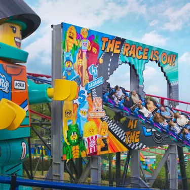 Families enjoying the rollercoaster Minifigure Speedway at the LEGOLAND Windsor Resort next to the giant Minifigure Roxie Racer