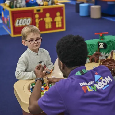 Child building with LEGO and interacting with staff member in the LEGOLAND Playroom
