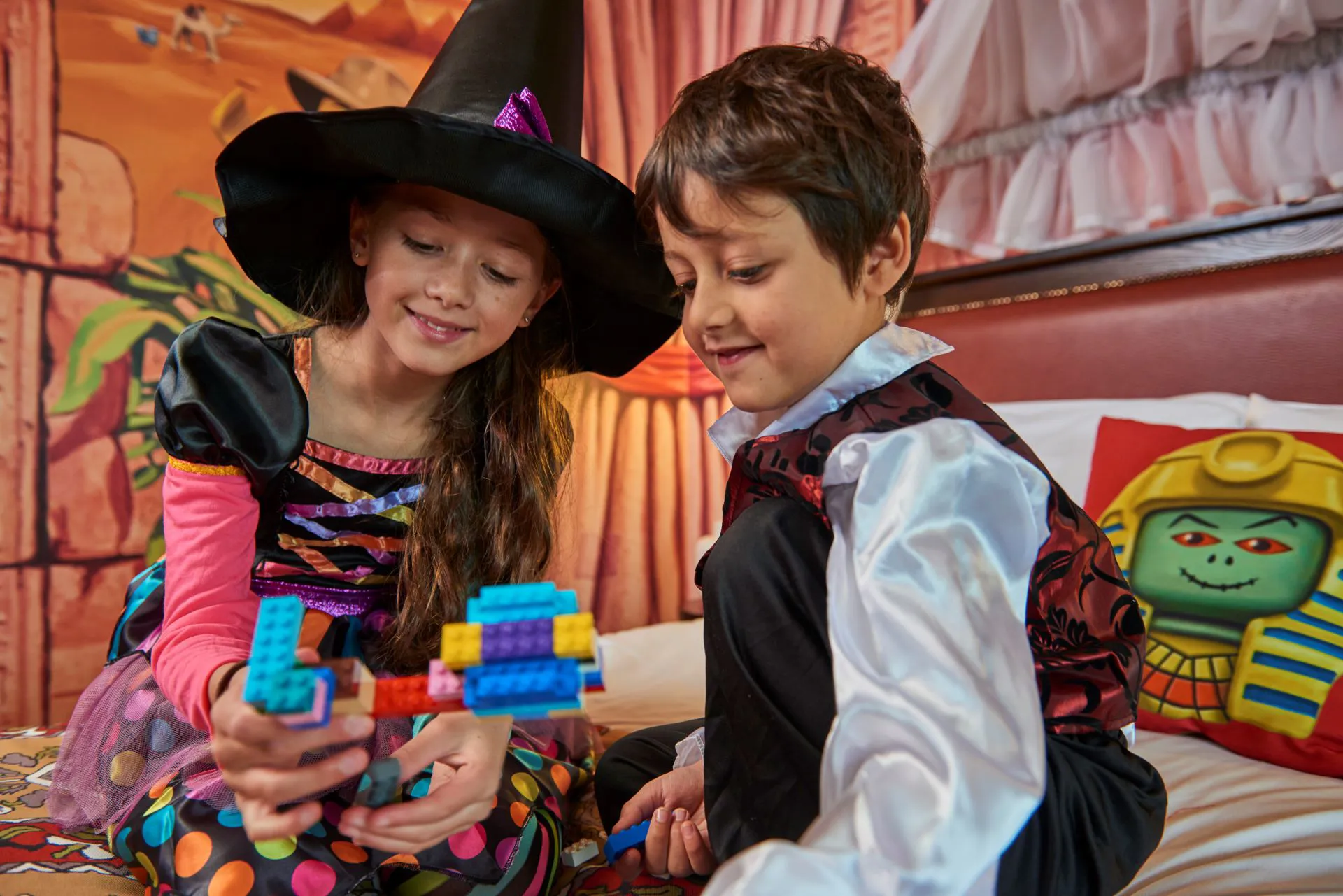 Little Boy and Girl dressed up in Halloween costumes sitting on a bed inside one of the LEGOLAND Windsor Resort Hotel themed rooms