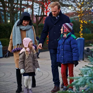 Family walking past snow covered Christmas trees and Christmas lights at LEGOLAND at Christmas
