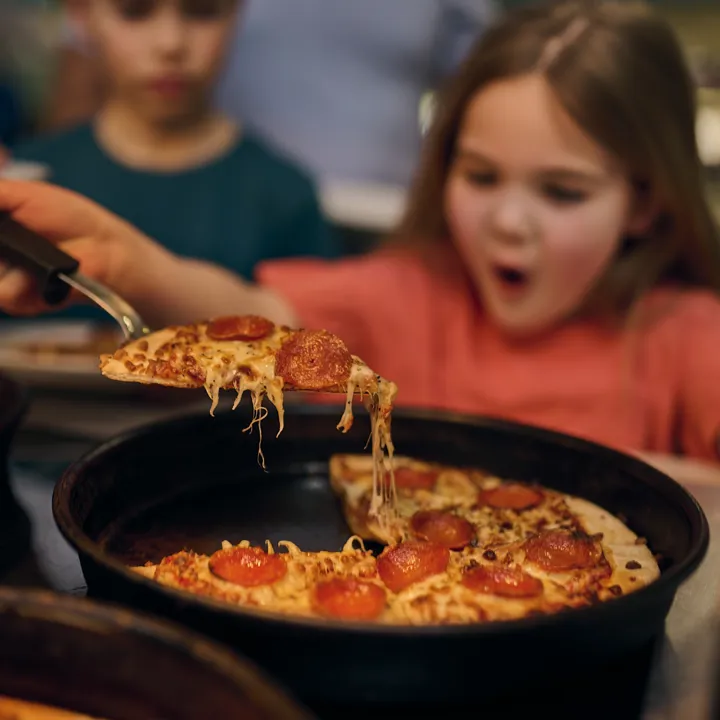 Young girl lifting slice of pepperoni pizza at City Walk Pizza & Pasta