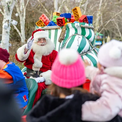 Father Christmas on a Sleigh waving, to a young woman and young girl both in pink hats