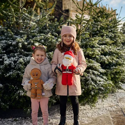 Two children holding plushies in front of snow covered trees