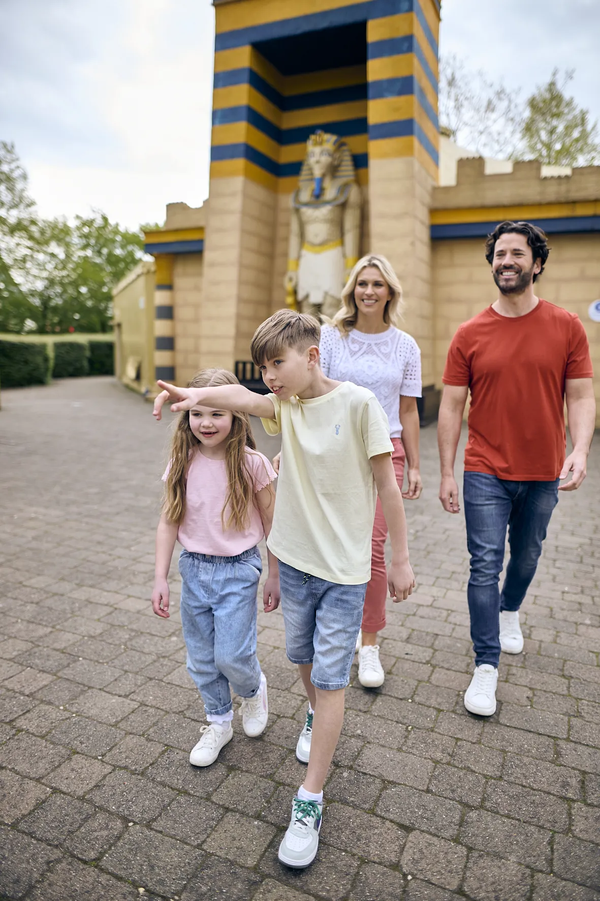 Boy pointing while talking to sister in Kingdom of the Pharaohs with parents and large LEGO model of Pharaoh in the background