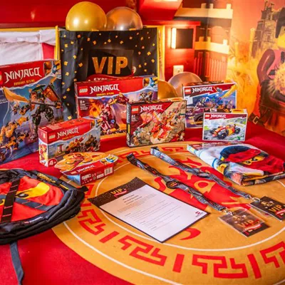 LEGO NINJAGO themed VIP Hotel Stay including LEGO NINJAGO sets, plush toys, bags, towels, VIP lanyards, a VIP Experiences bag, balloons and more on a bed in a LEGO NINJAGO themed room